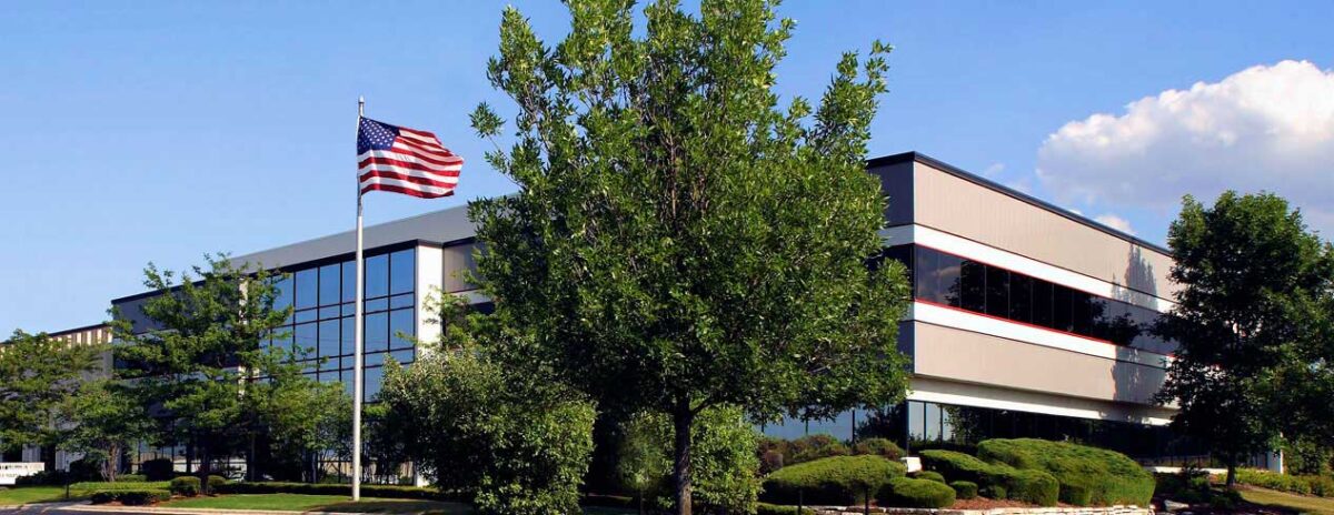 A large building with an American flag flying in front on a sunny day.